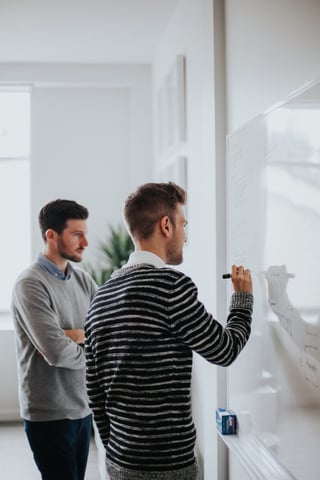 Two men at a whiteboard reviewing data. A live chat widget coupled with a simple CRM can produce actionable data. Photo by Jonathan Velasquez on Unsplash (https://unsplash.com)