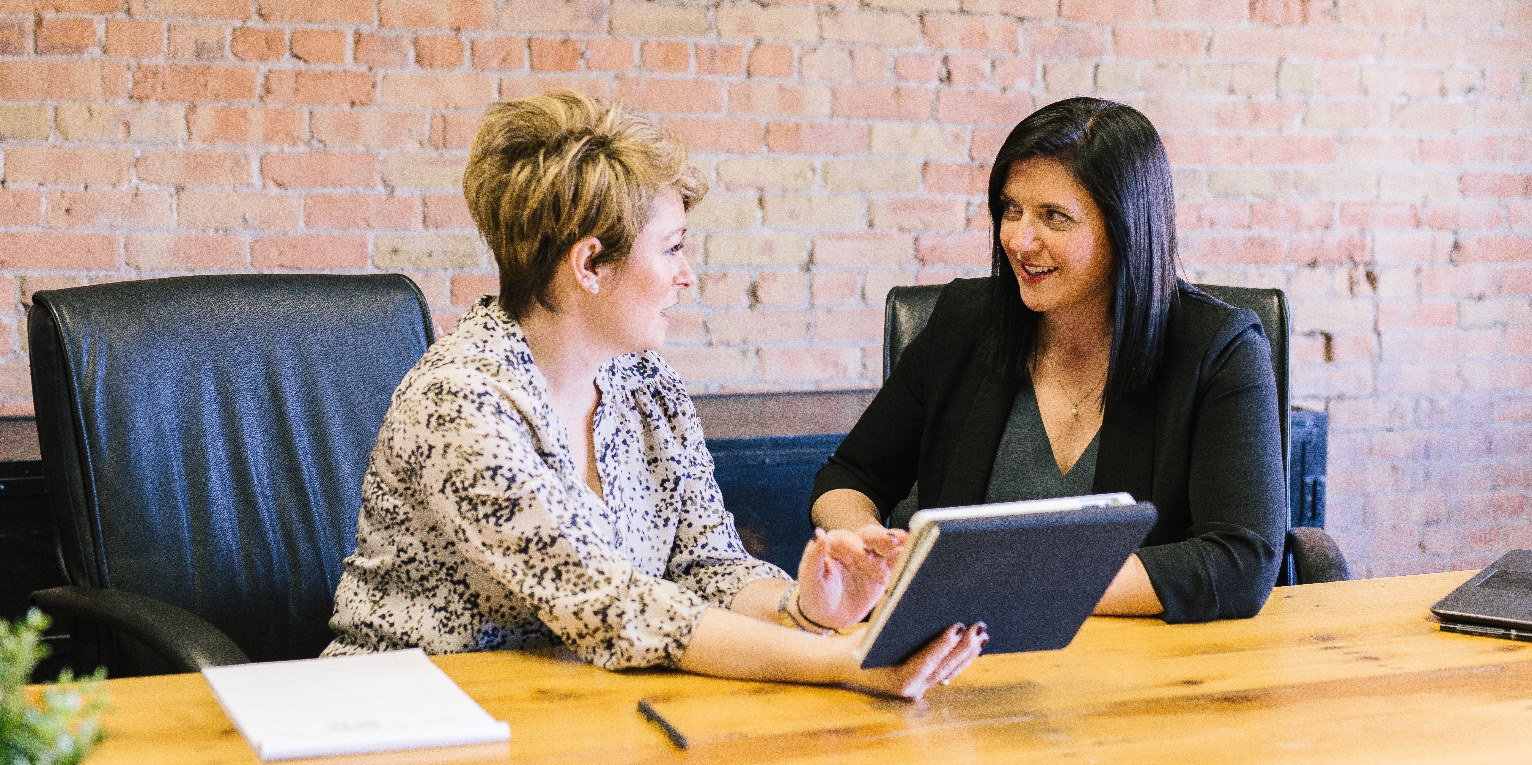 Two women at a table look at a digital tablet together