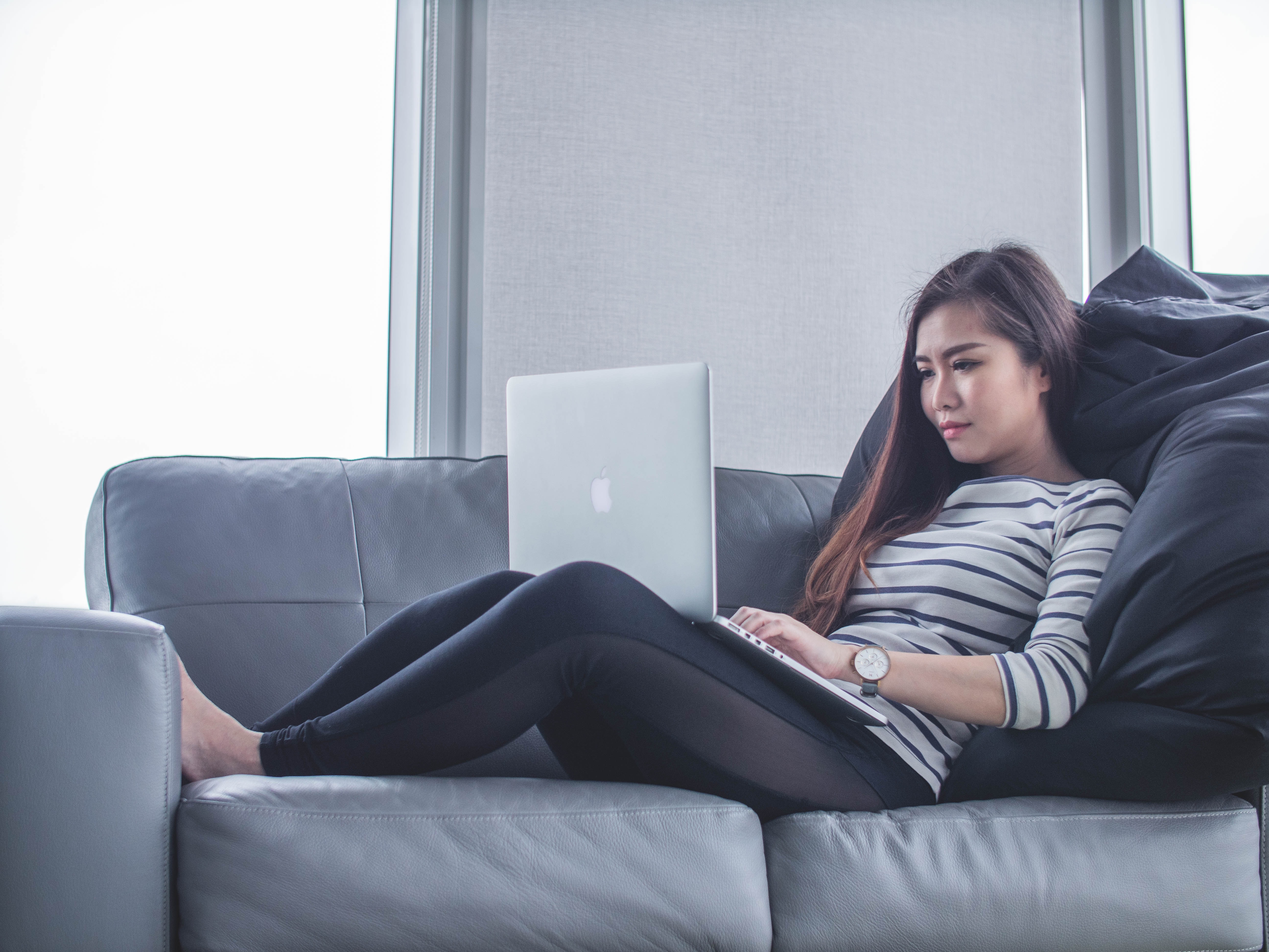 A woman on a couch is typing on her laptop